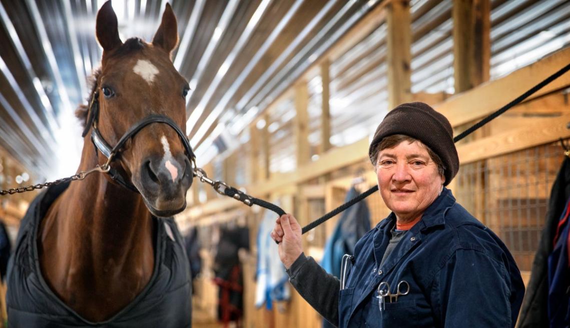A woman holds the reigns of a horse as she poses for a photo