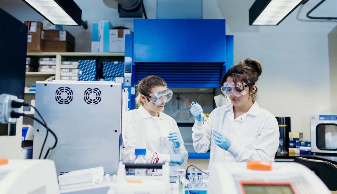 two students in lab coats work in a lab