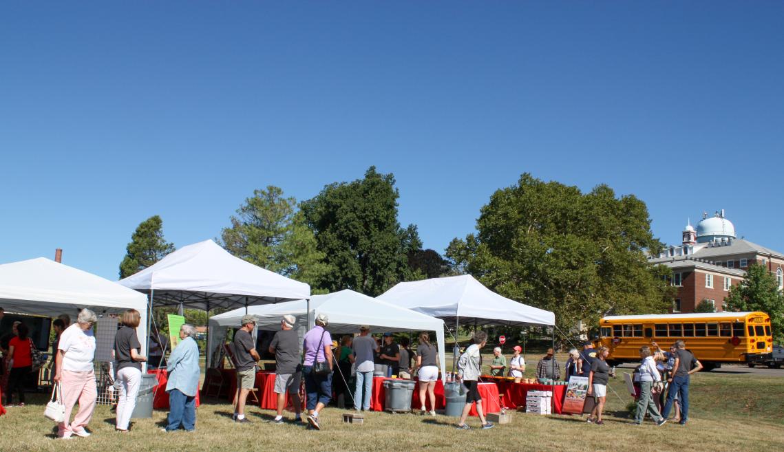 People gathered underneath white tents and red tablecloths.