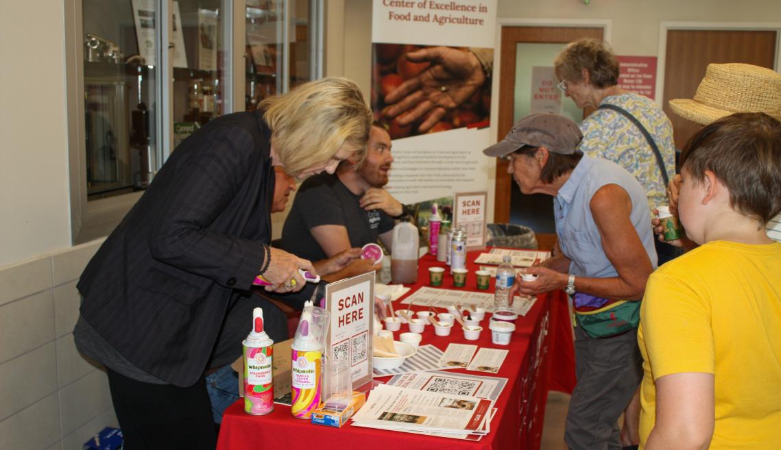 People gathered around a red table with free samples of food and drinks. 