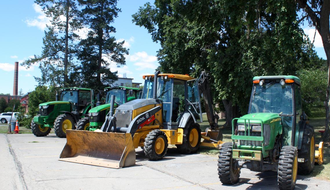 Tractors and other farm equipment lined up on display along a road. 