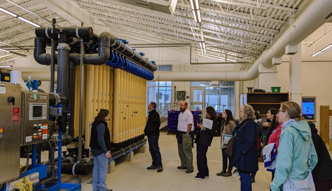 Photograph of a group of people on a tour looking at large vats in an industrial styled interior room.