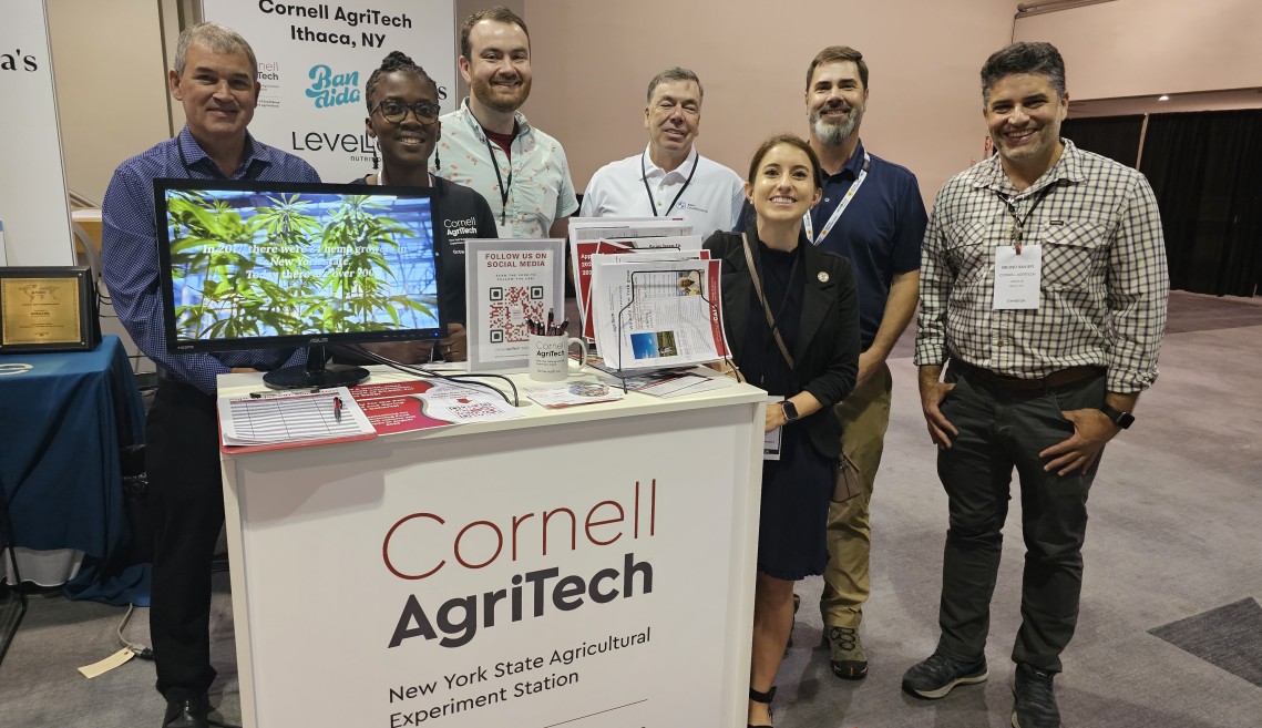 A group of seven people in front of a booth that says Cornell AgriTech New York State Agricultural Experiment Station