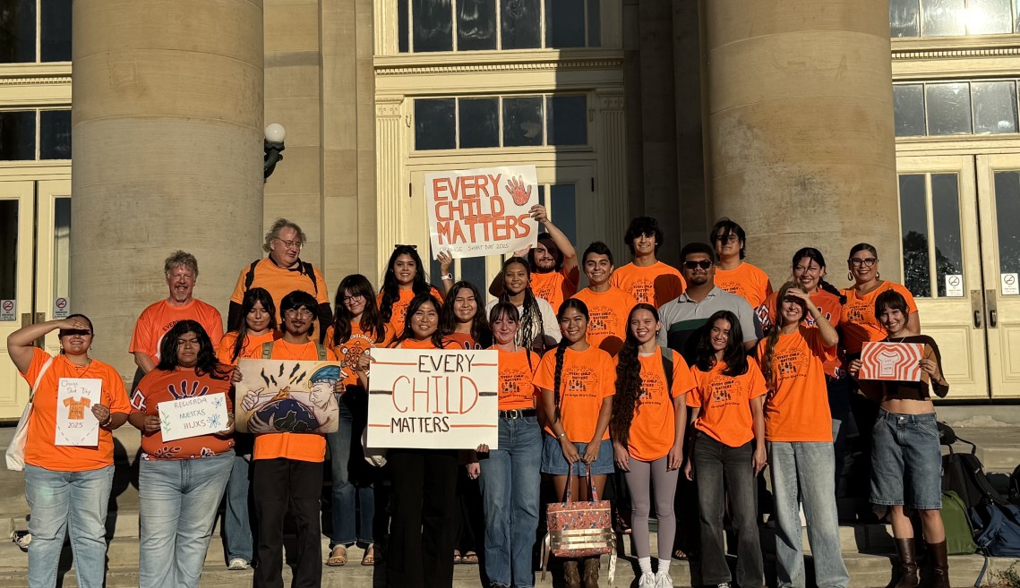 Students in orange shirts stand outside Goldwin Smith.