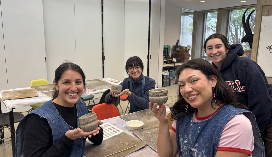 Students smile holding ceramic pots.