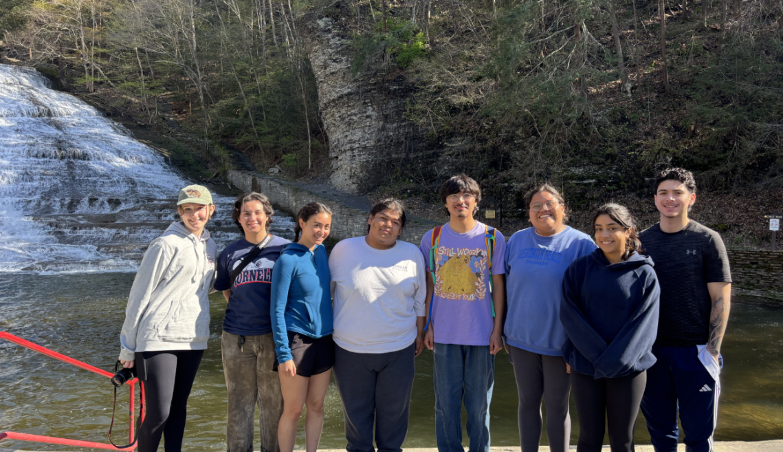 Students smile for a group photo in front of a waterfall.