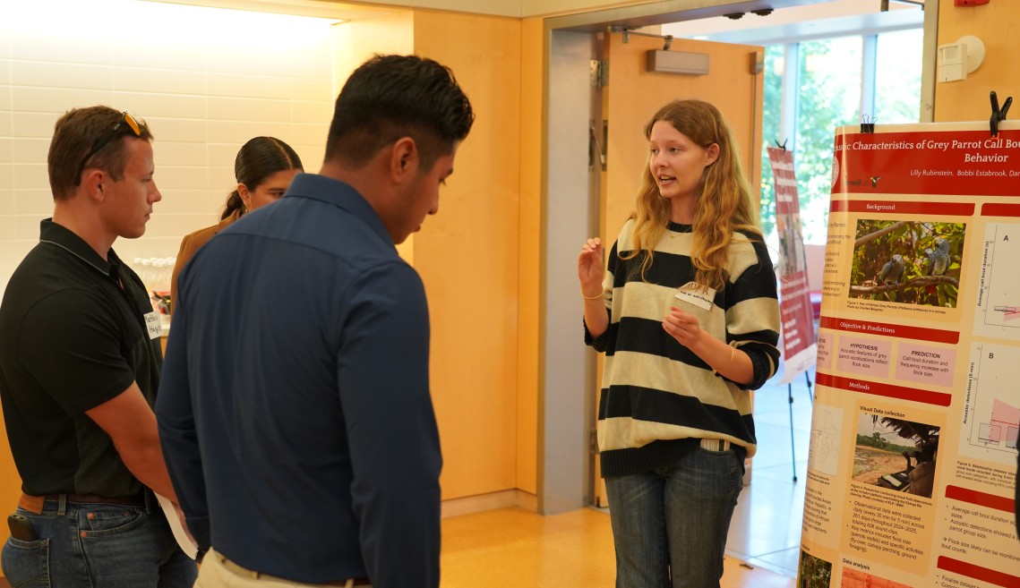 A woman talks to two men in front of a research poster.