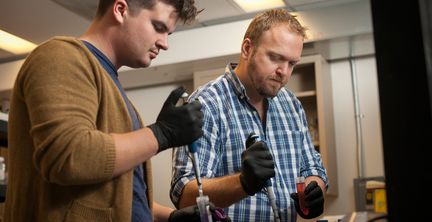 two men with gloved hands work in a lab