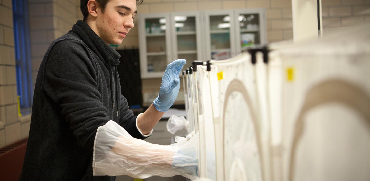 a student puts a gloved hand into a machine