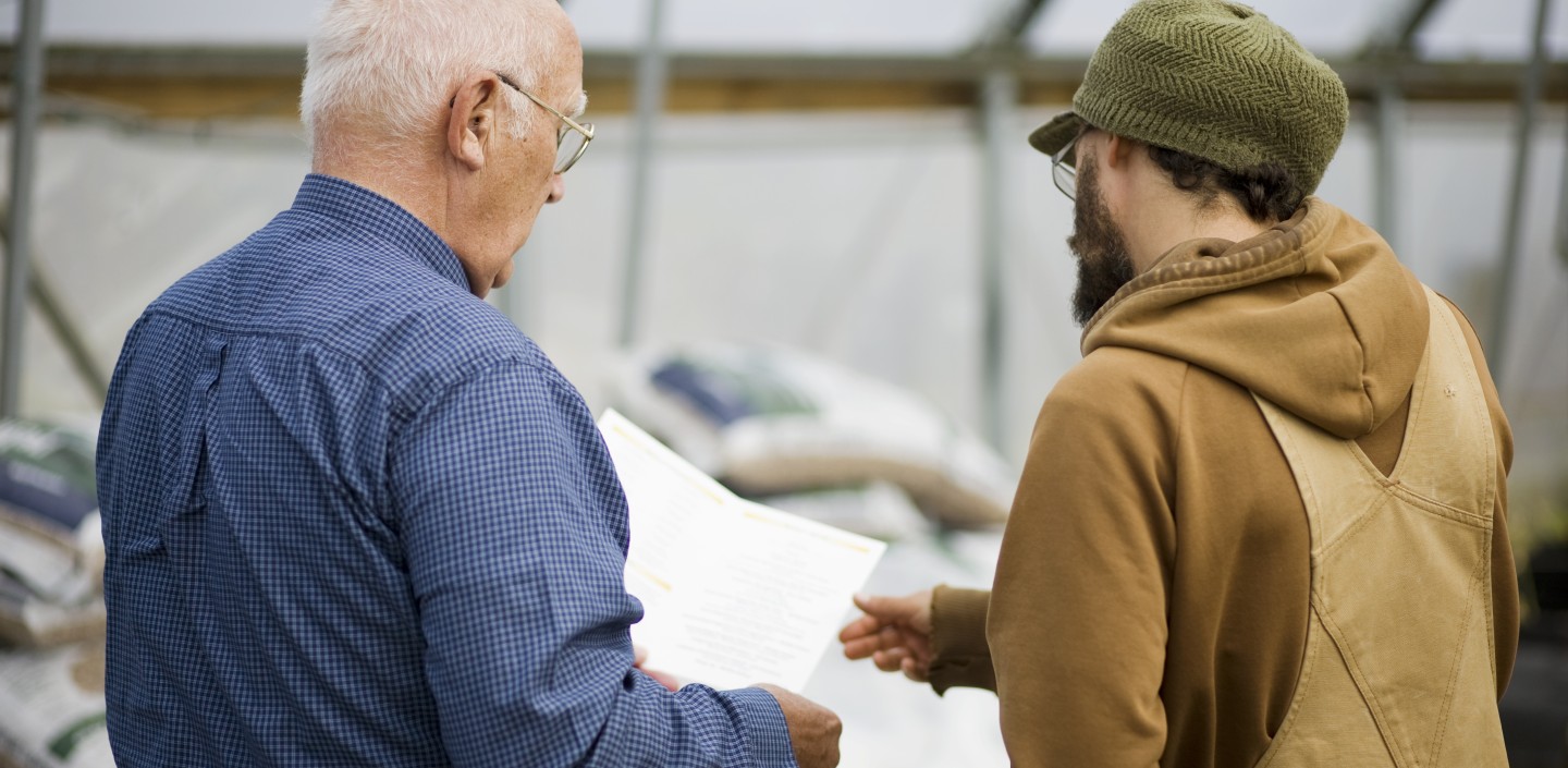 Two people looking over a piece of paper in a greenhouse.