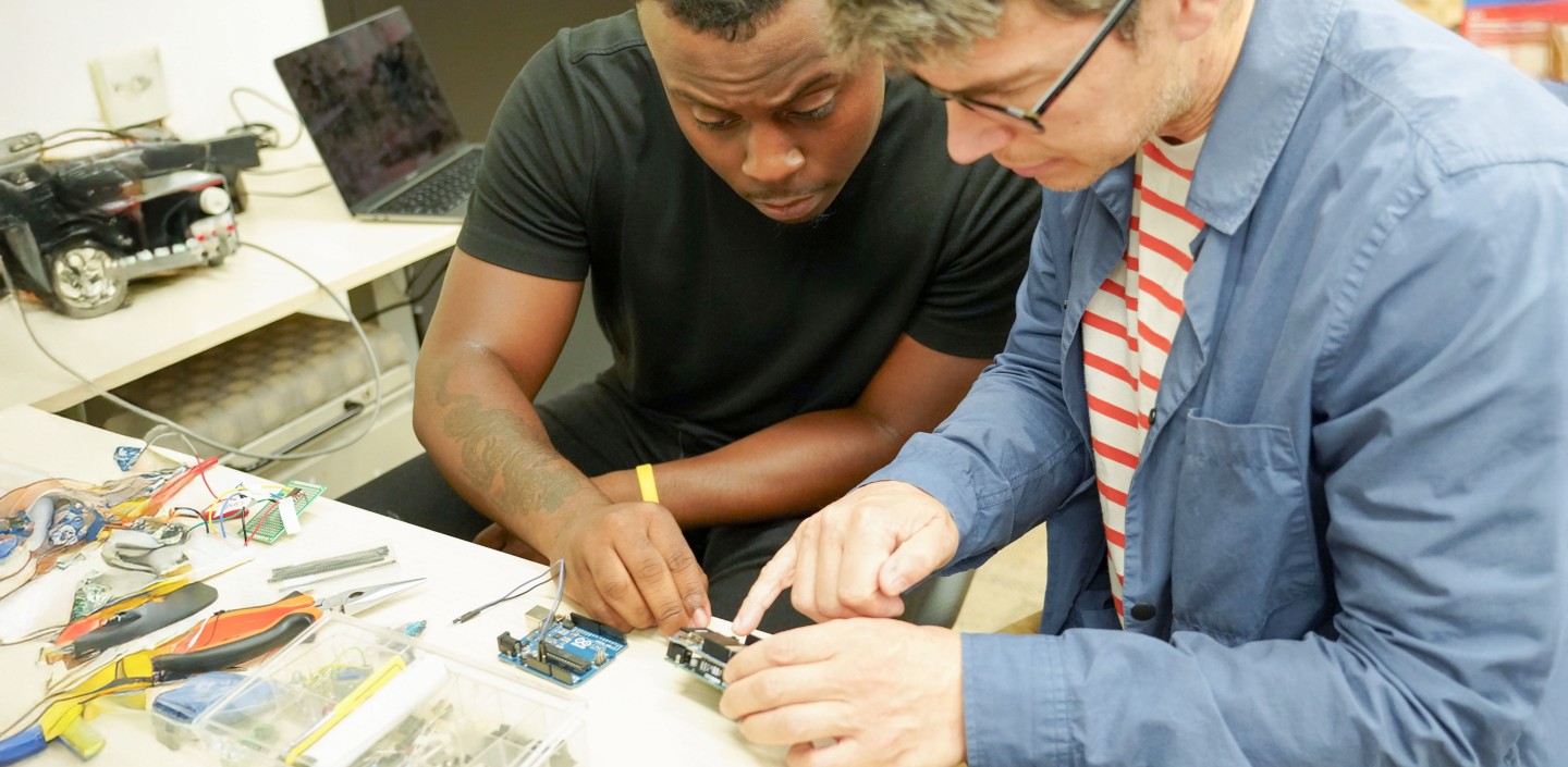 two men look at a piece of tech in a lab