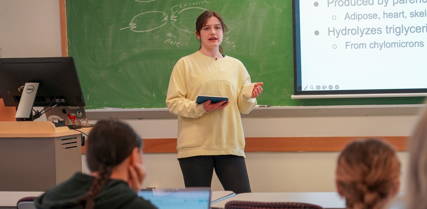 a woman stands in front of a class and talks