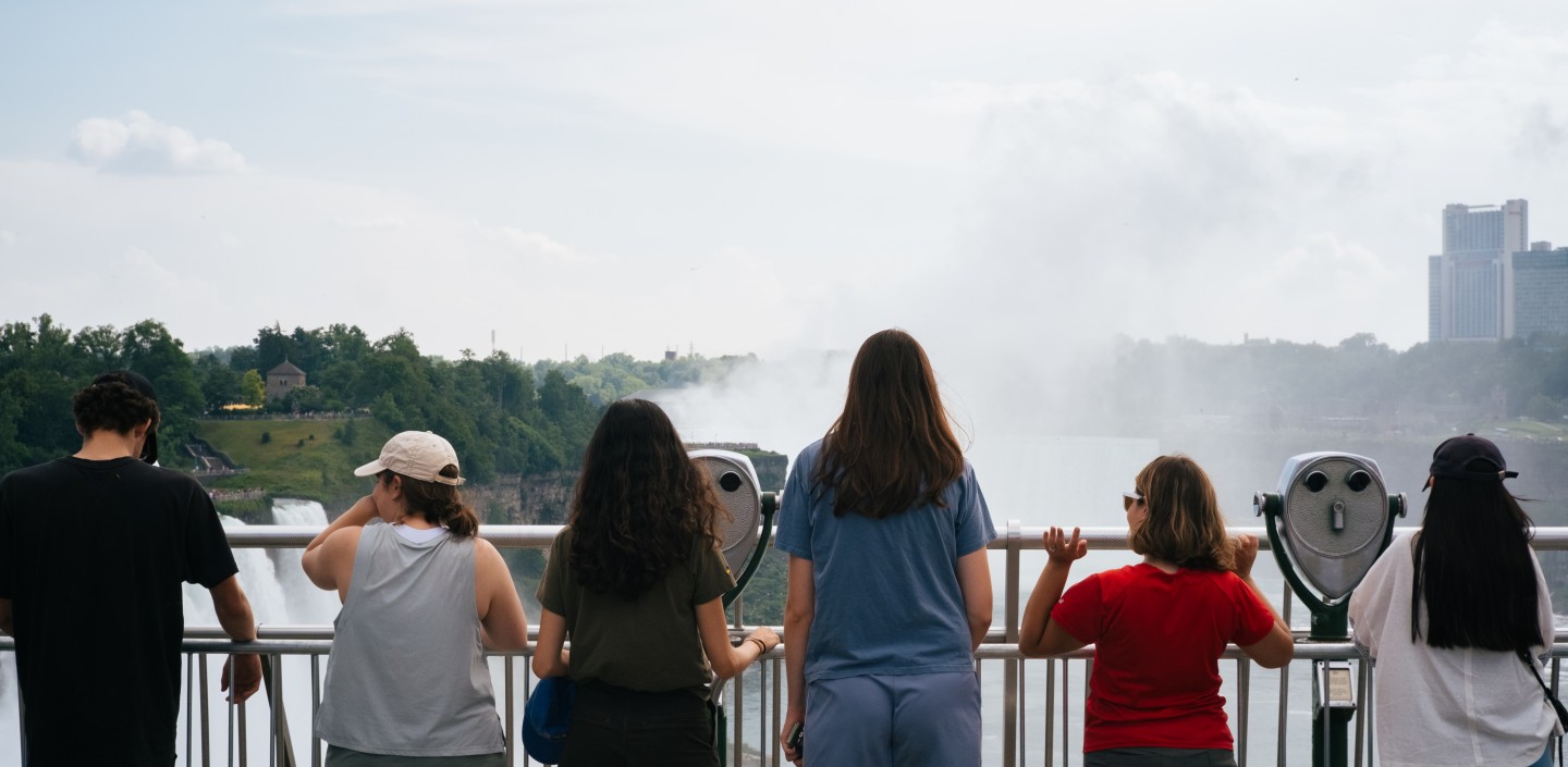 Photograph of a group of six people standing looking over a railing at Niagara Falls.