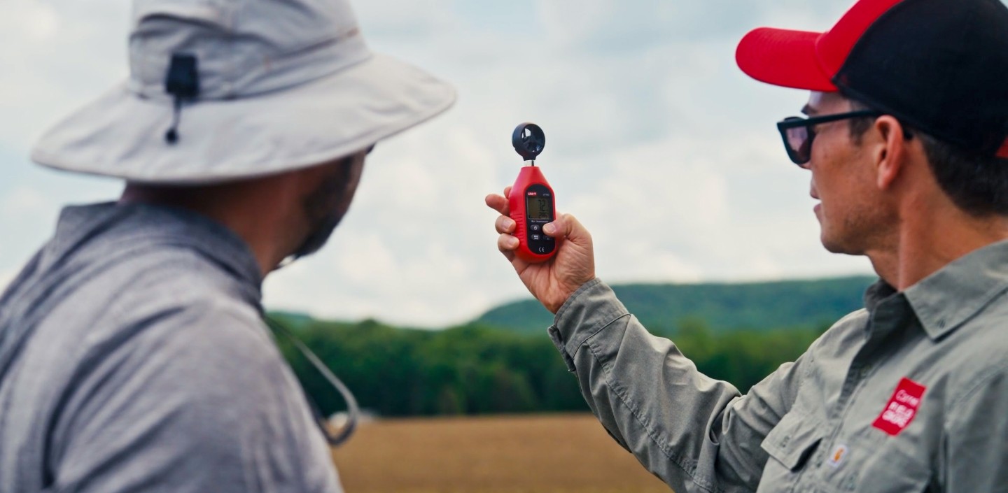 two men hold up a piece of tech in a field