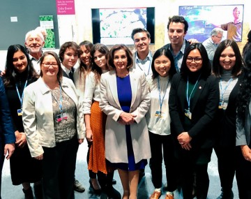 A group of male and female students standing and smiling with an older woman standing in the center of them