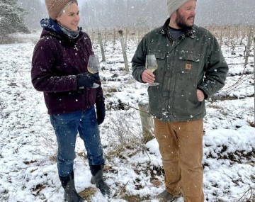 Two people standing outside in the snow with glasses of white wine