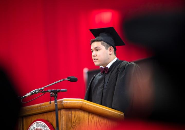 A student standing at a podium in a graduation cap and gown