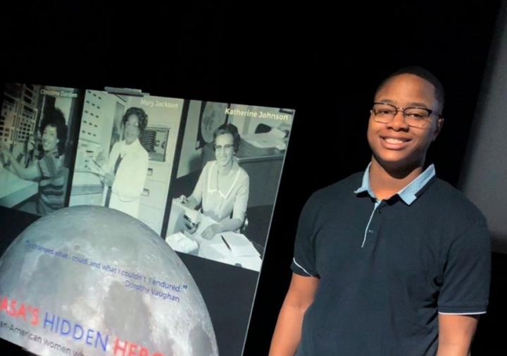 A male student standing next to a poster