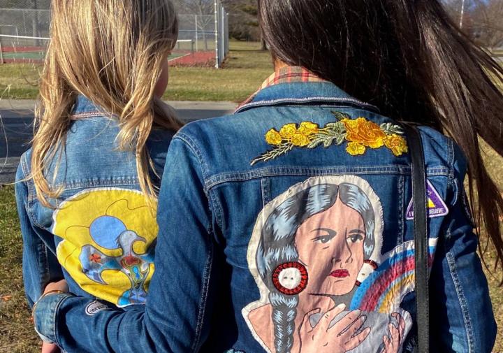 Two females with their backs to the camera wearing jean jackets with applique beadwork on them.