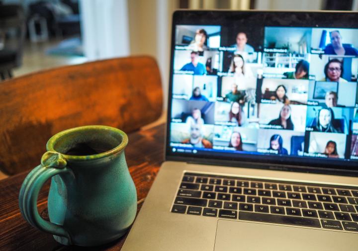 A zoom call pulled up on a laptop with a green mug next to it on the table