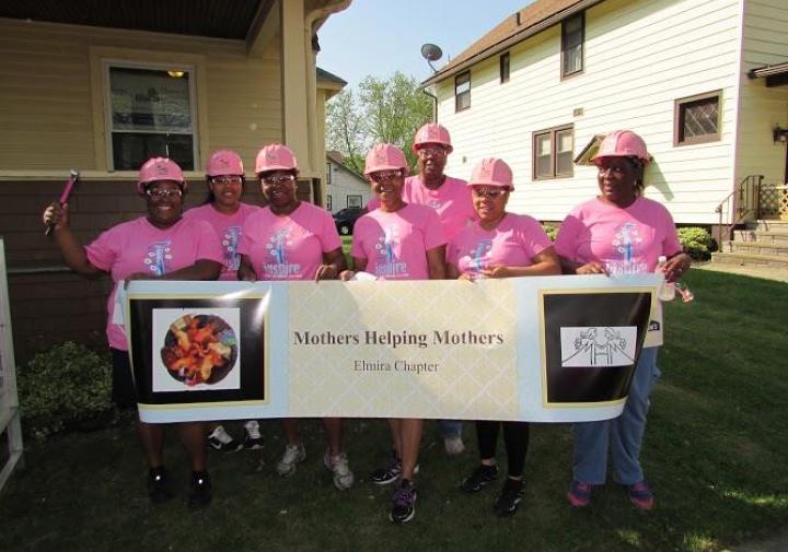 Group of mothers stands holding banner and wearing construction hats