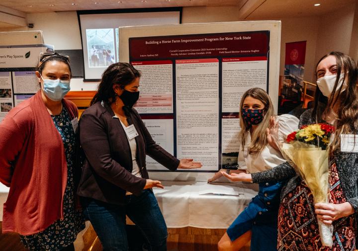 Four masked people stand in front of a poster display. They smile with their eyes.