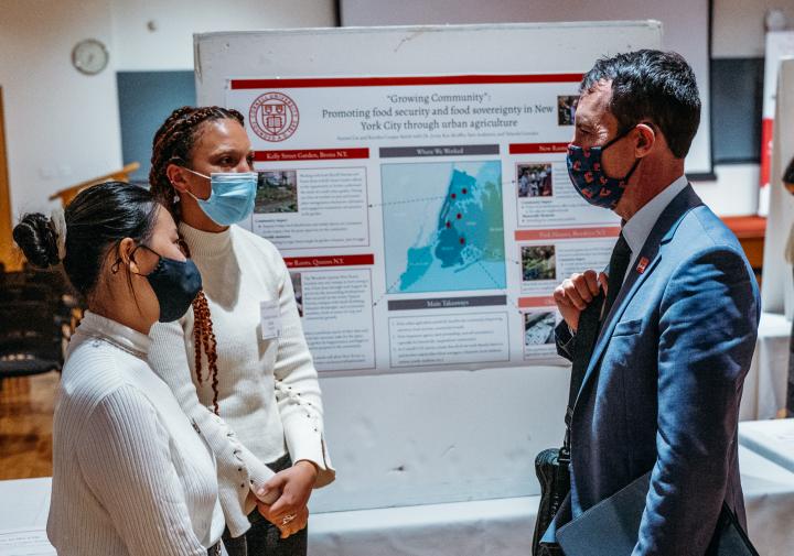 Three people talk to each other in front of a poster display