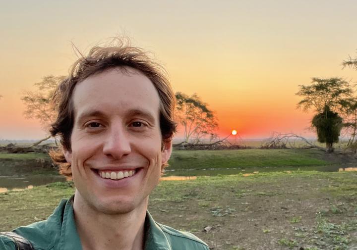 Person in a green buttin down standing outside while the sun is setting