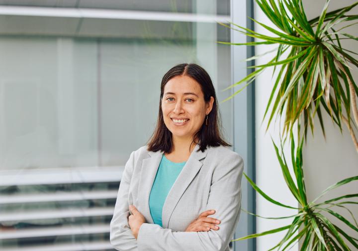 Person in a turquoise shirt and grey blazer standing in front of a window 