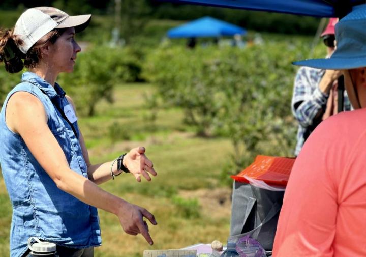 Anna Wallis gesturing towards her table demonstrating moth traps, speaking to two adults