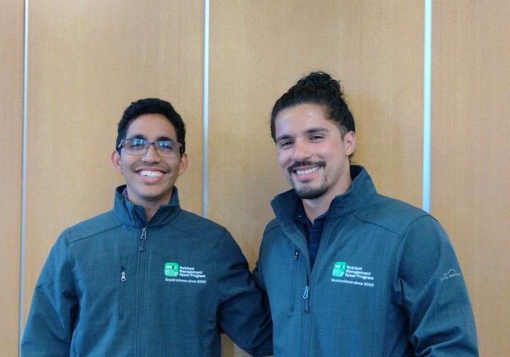 Two men stand next to each other, smiling.