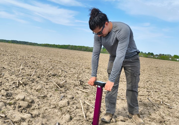 A man is bent over a tool in a field, pushing the tool in the ground.