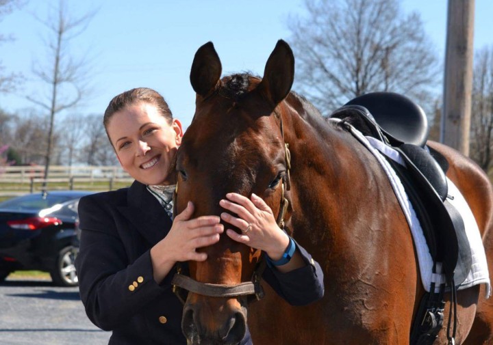 A headshot photo of Erika Machtinger smiling and standing with a brown horse