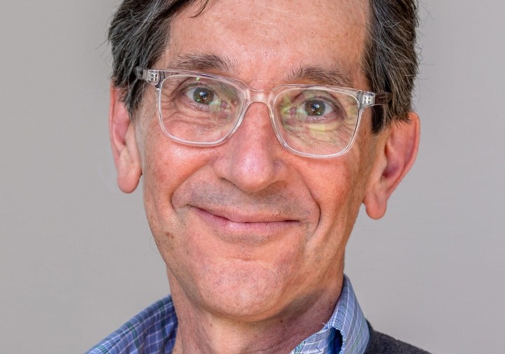 Professional portrait of a person wearing glasses, a blue shirt and grey sweater.