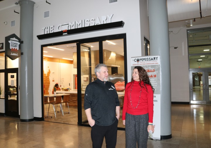 A man and a woman standing together in front of a room with a sign that reads "The Commissary"
