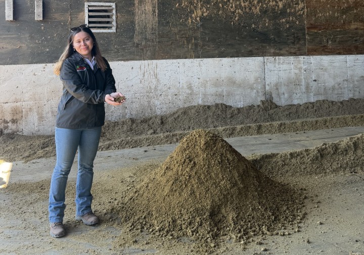 A woman holds soil and stands next to a large pile of soil.