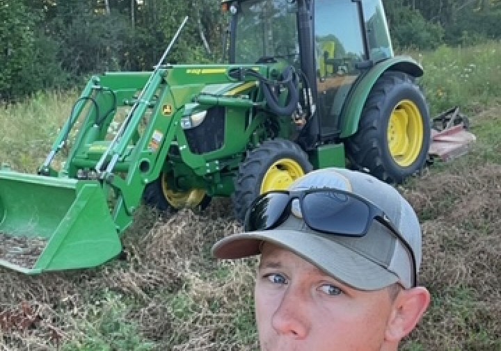A man poses in the field with farm equipment.