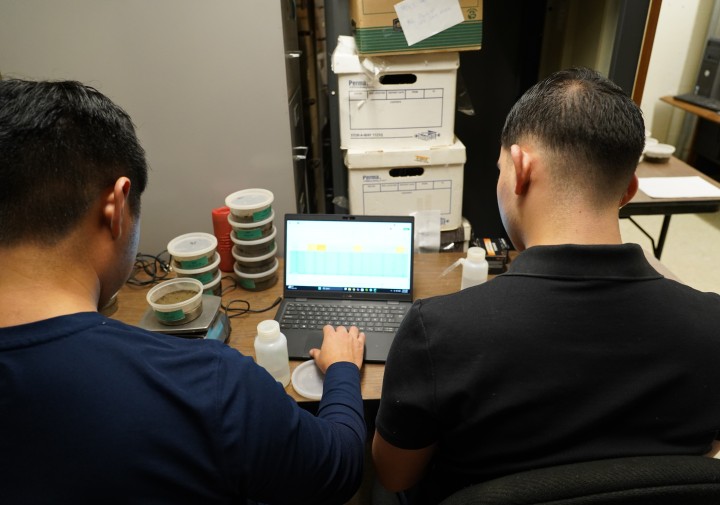 Two men sit at a desk working in a lab.