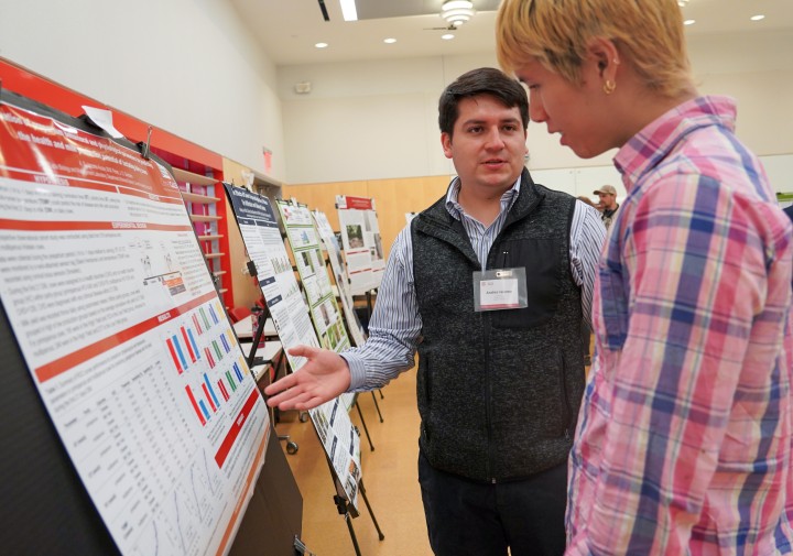 a man gestures at an academic poster while another man watches