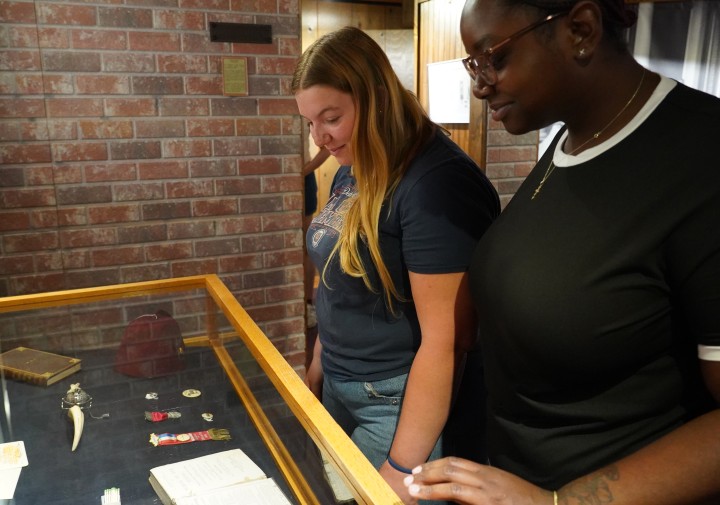Two women look towards items in a glass case.