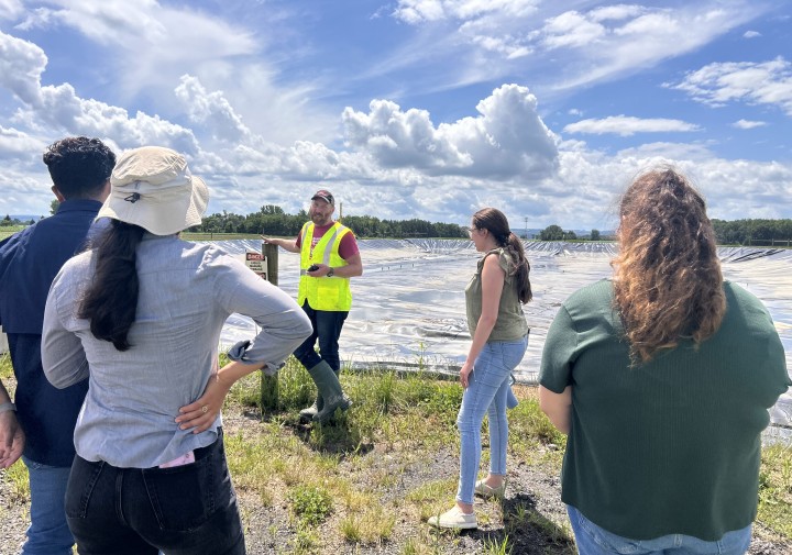 A man talks to a group of people while standing in front of a covered manure pit.