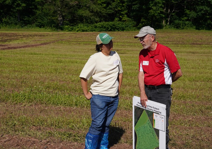 A woman stands to the left of a man in a field, talking.