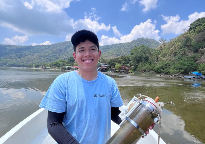 A man stands in a floating boat and holds a jar of dirty water.