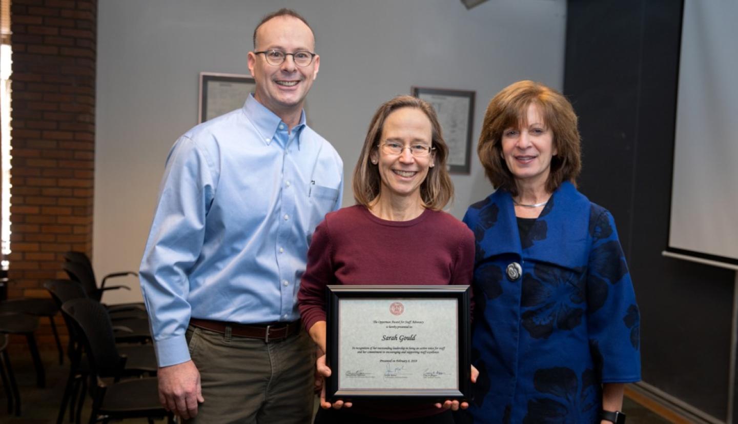 staff members stand with award winner holding plaque