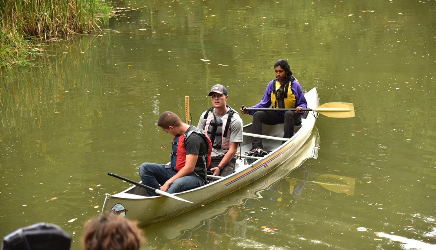 Three students sit in a canoe