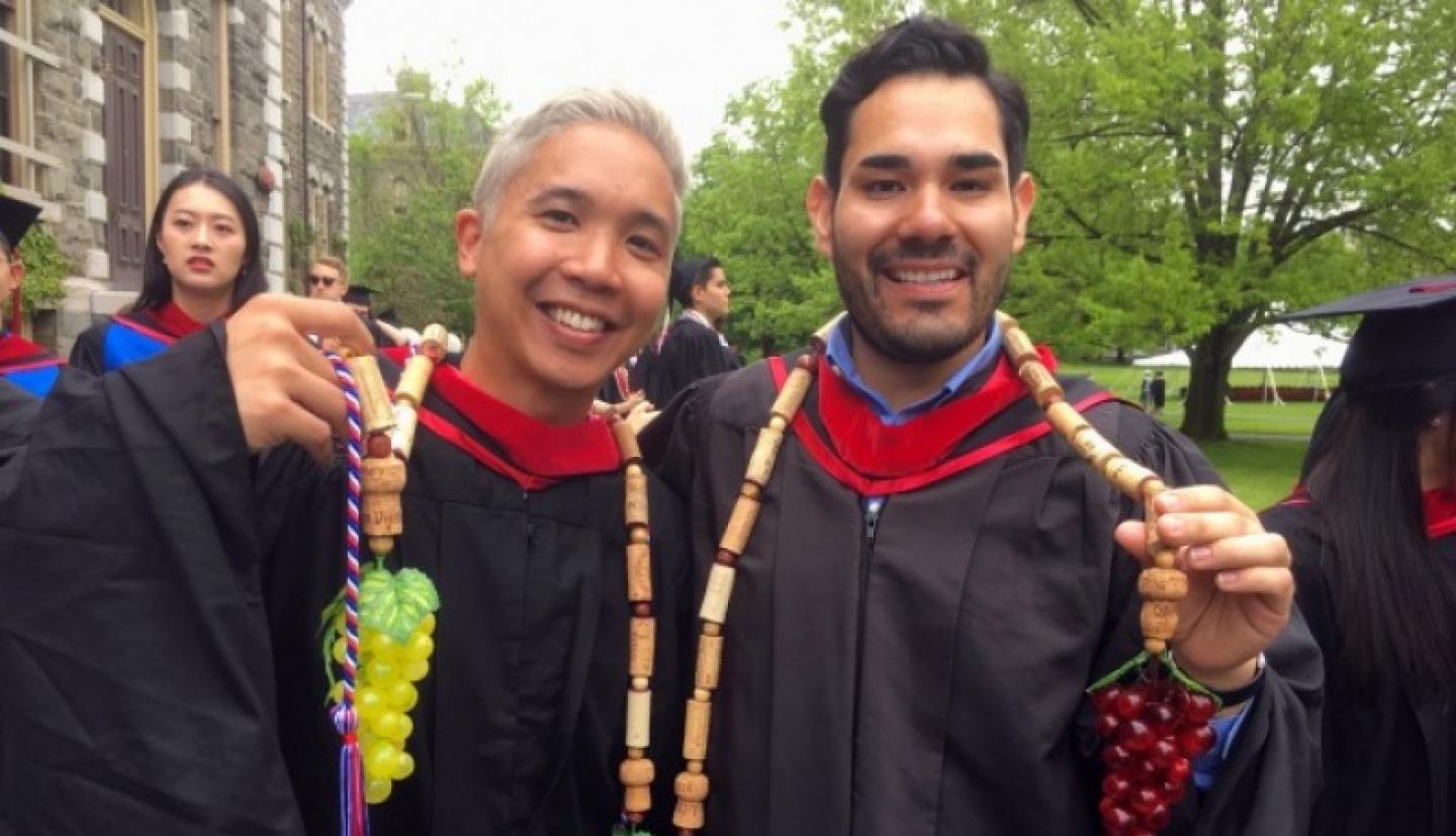 Two graduating students show off cords made of wine corks and plastic grapes