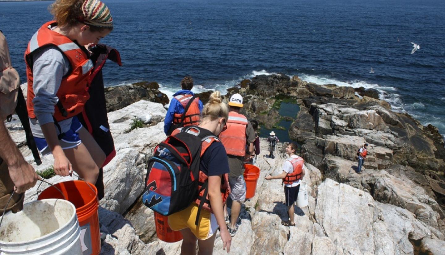Students climb down rocks to get to ocean