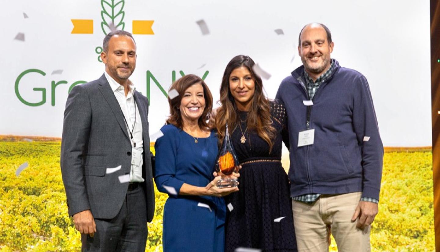 Two women and two men standing on a stage holding a trophy with confetti falling around them