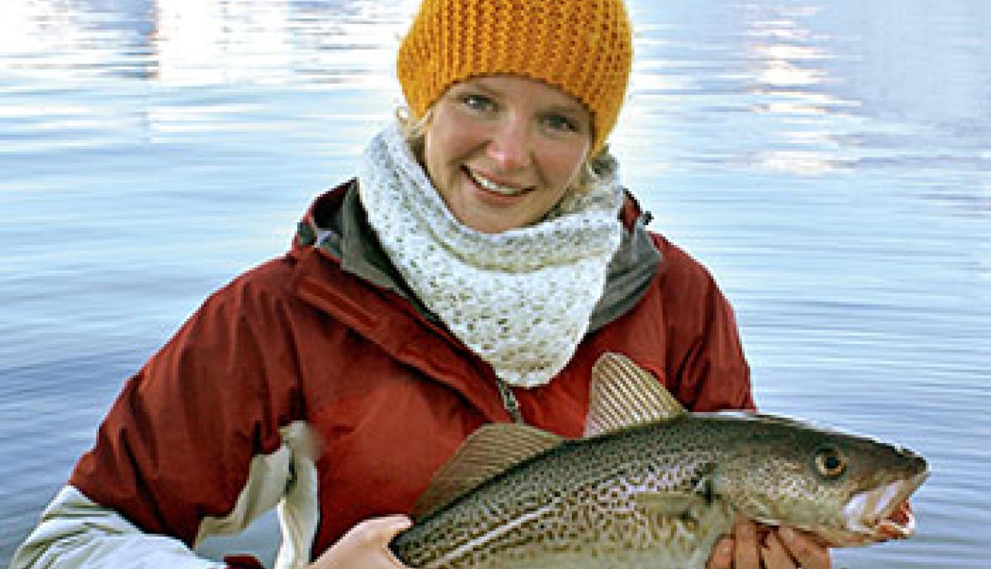 A woman holds a fish on a boat