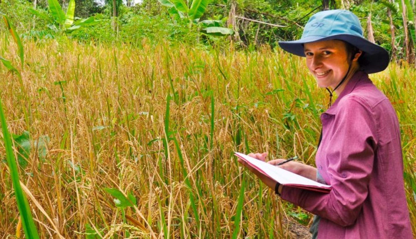 Female student stands with clip board in a field.